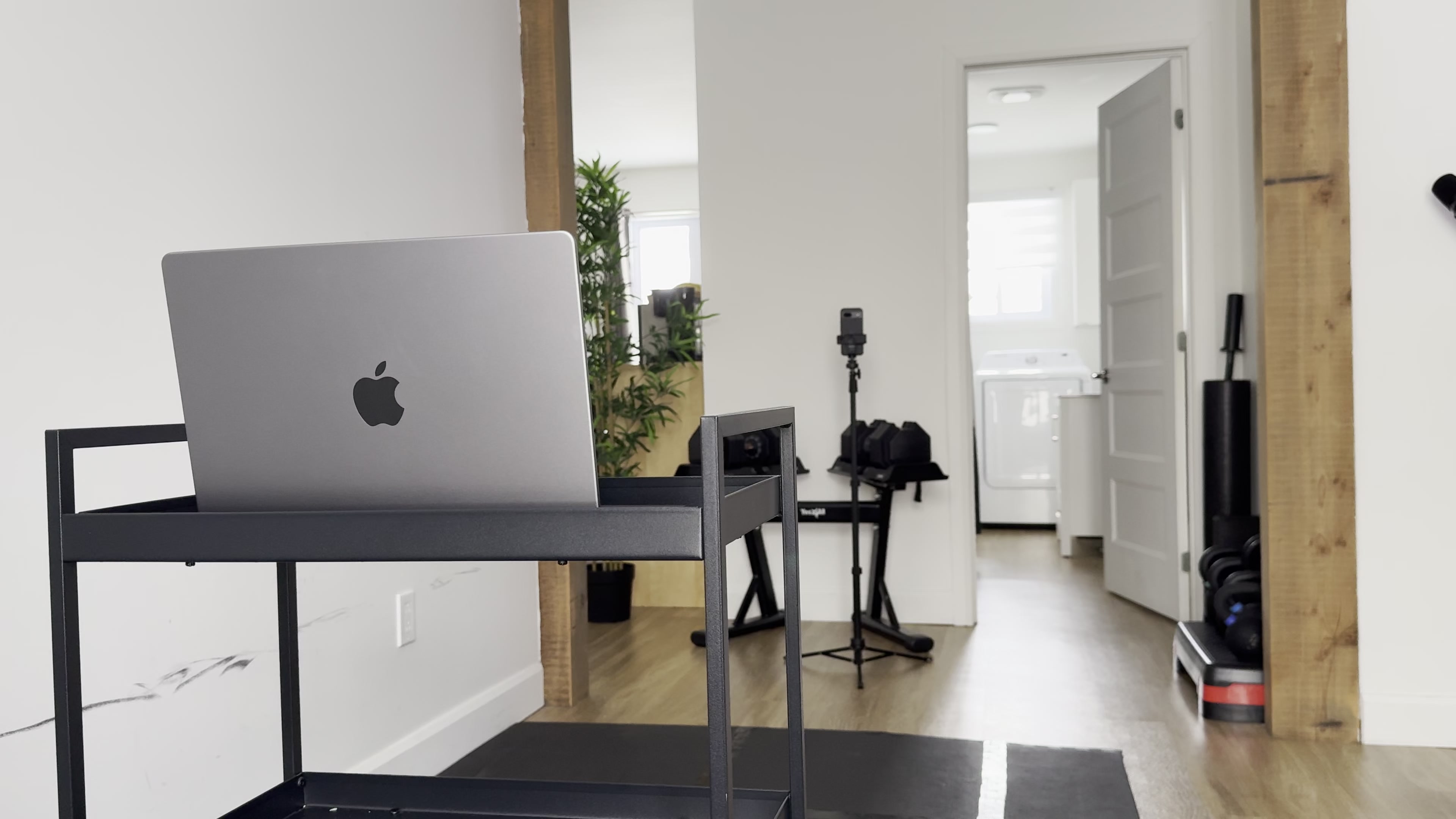 Home physical therapy setup with laptop, phone on tripod, and open exercise space